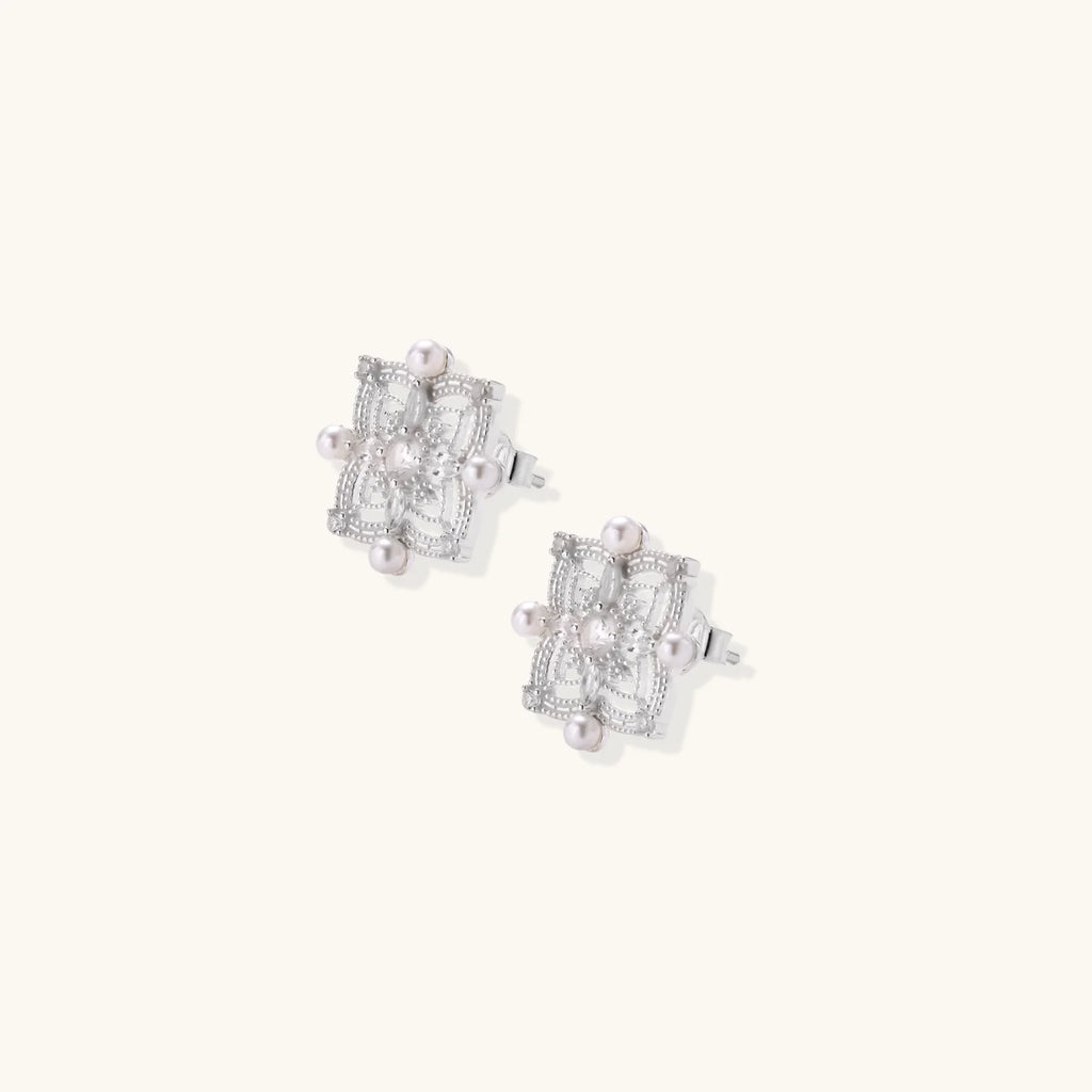 Ornate sterling silver stud earrings with mandala-inspired filigree pattern and four freshwater pearls on beige background