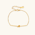 Delicate gold chain bracelet with minimalist bar and centered knot detail on cream background