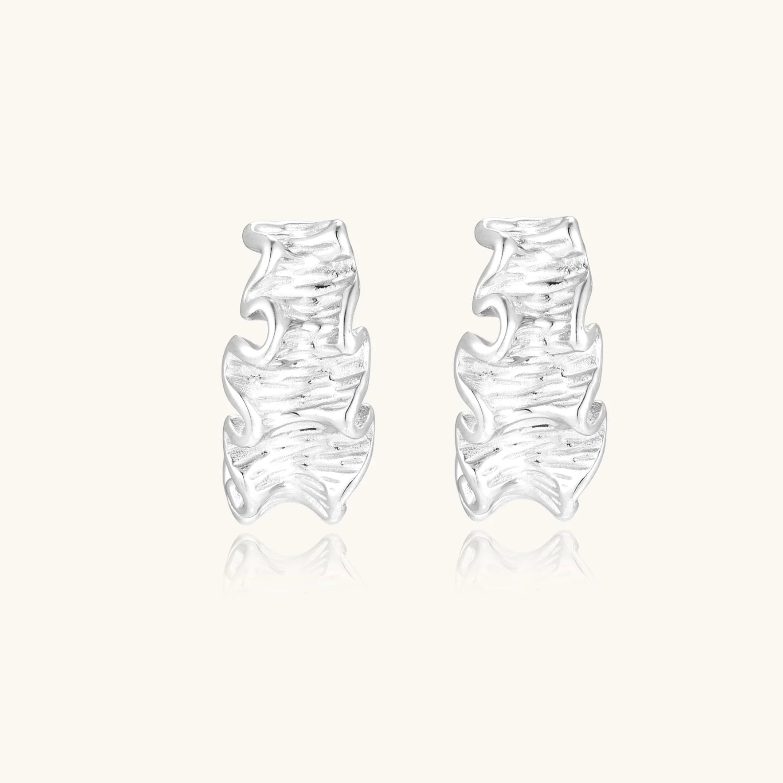 White gold plated sculptural hoop earrings with organic wavy edges and reflective metallic finish on cream background