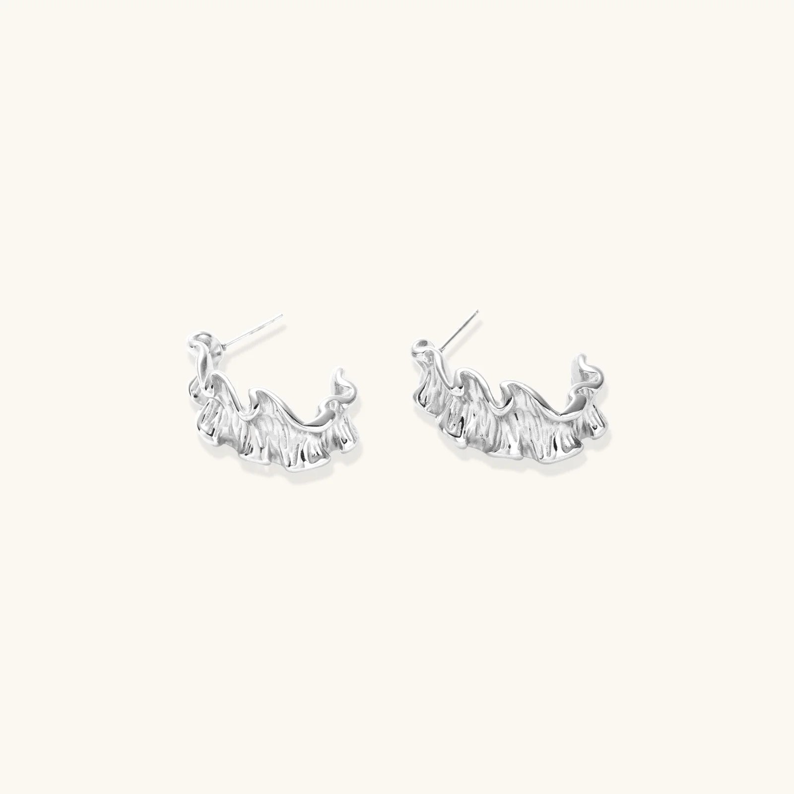 White gold plated sculptural hoop earrings with organic wavy edges and reflective metallic finish on cream background