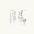 White gold plated sculptural hoop earrings with organic wavy edges and reflective metallic finish on cream background
