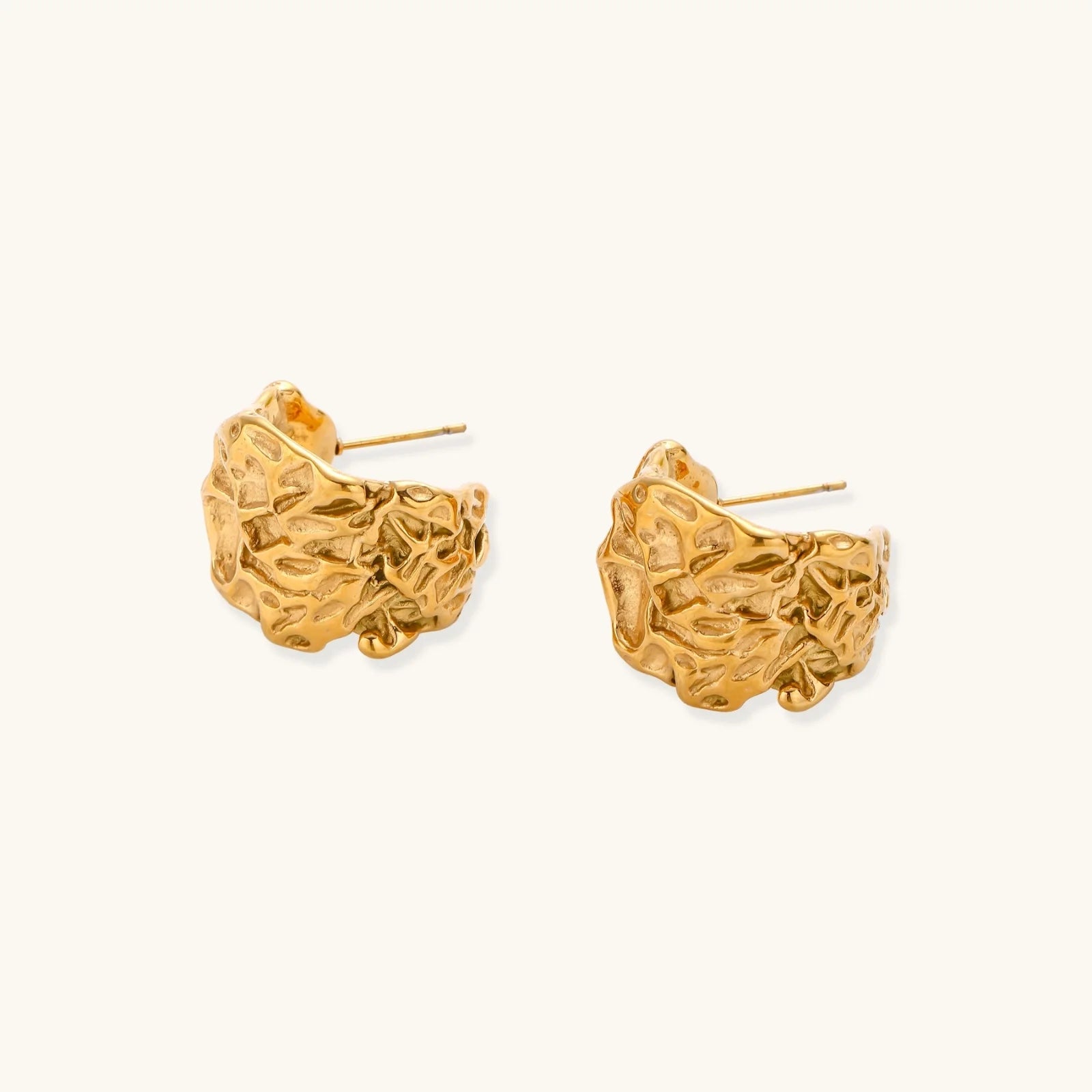 Sculptural gold-plated hoops with organic crushed texture on cream background