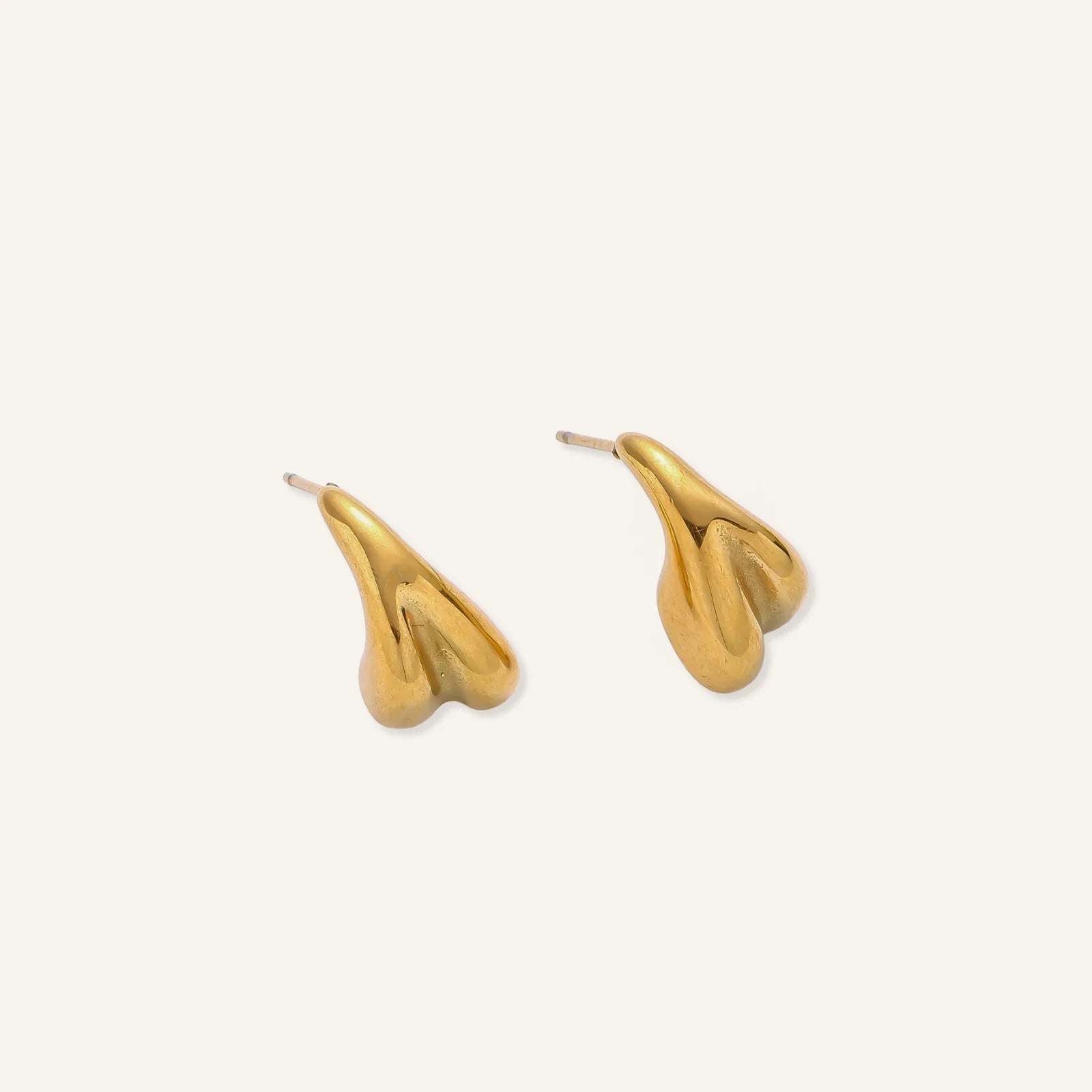 Pair of sculptural gold stud earrings with twisted organic forms on cream background